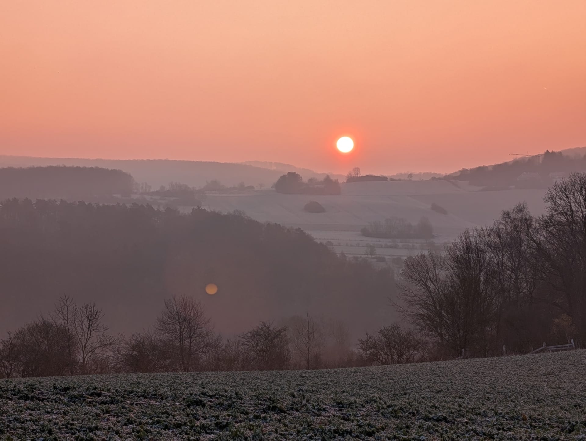 Roter Sonnenaufgang über nebligen, raureifbedeckten Hügeln und Feldern im Bratental, kahle Bäume als Silhouetten.