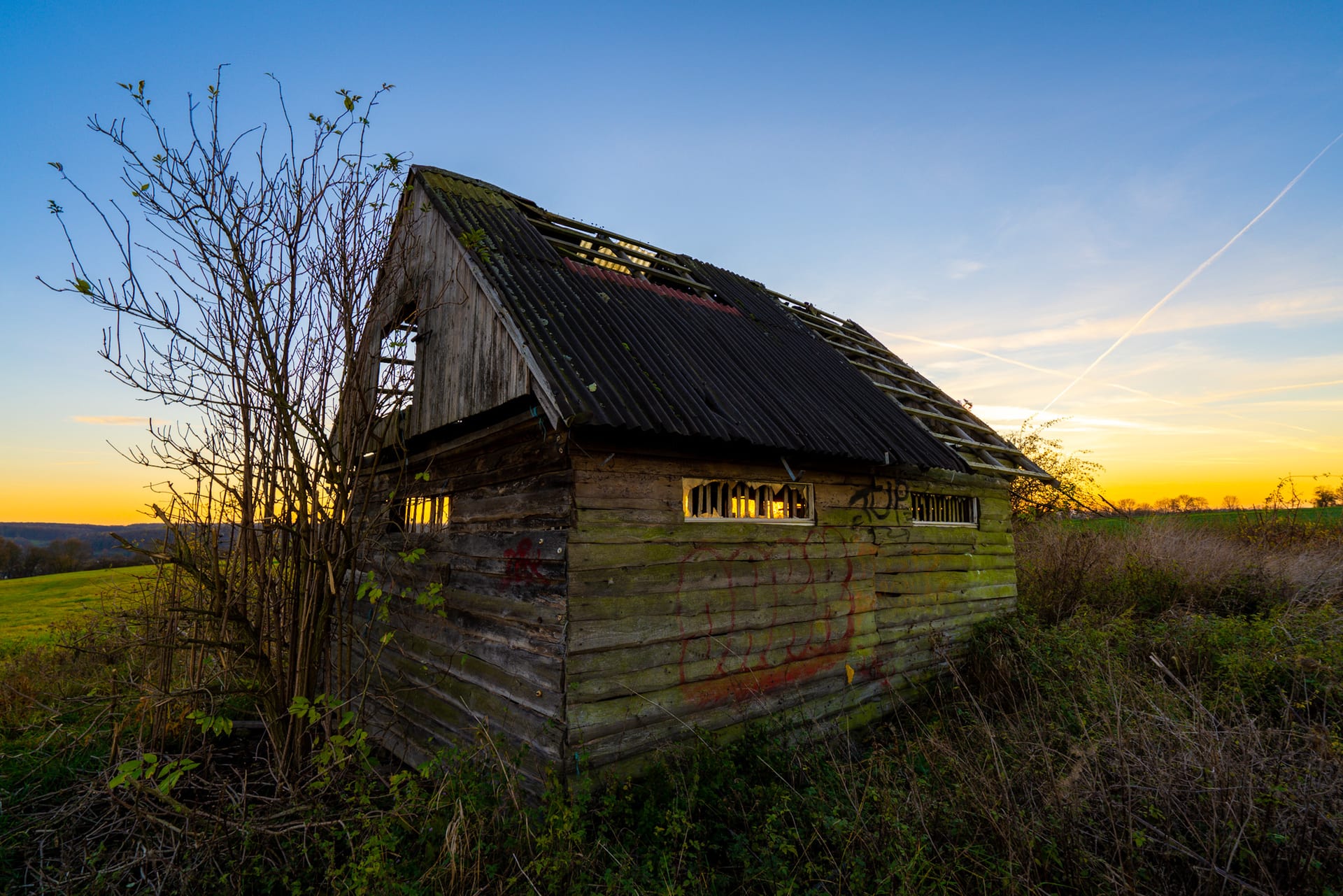 Verfallene Holzscheune mit Wellblechdach auf einem Feld bei Nikolausberg im farbigen Sonnenuntergang.