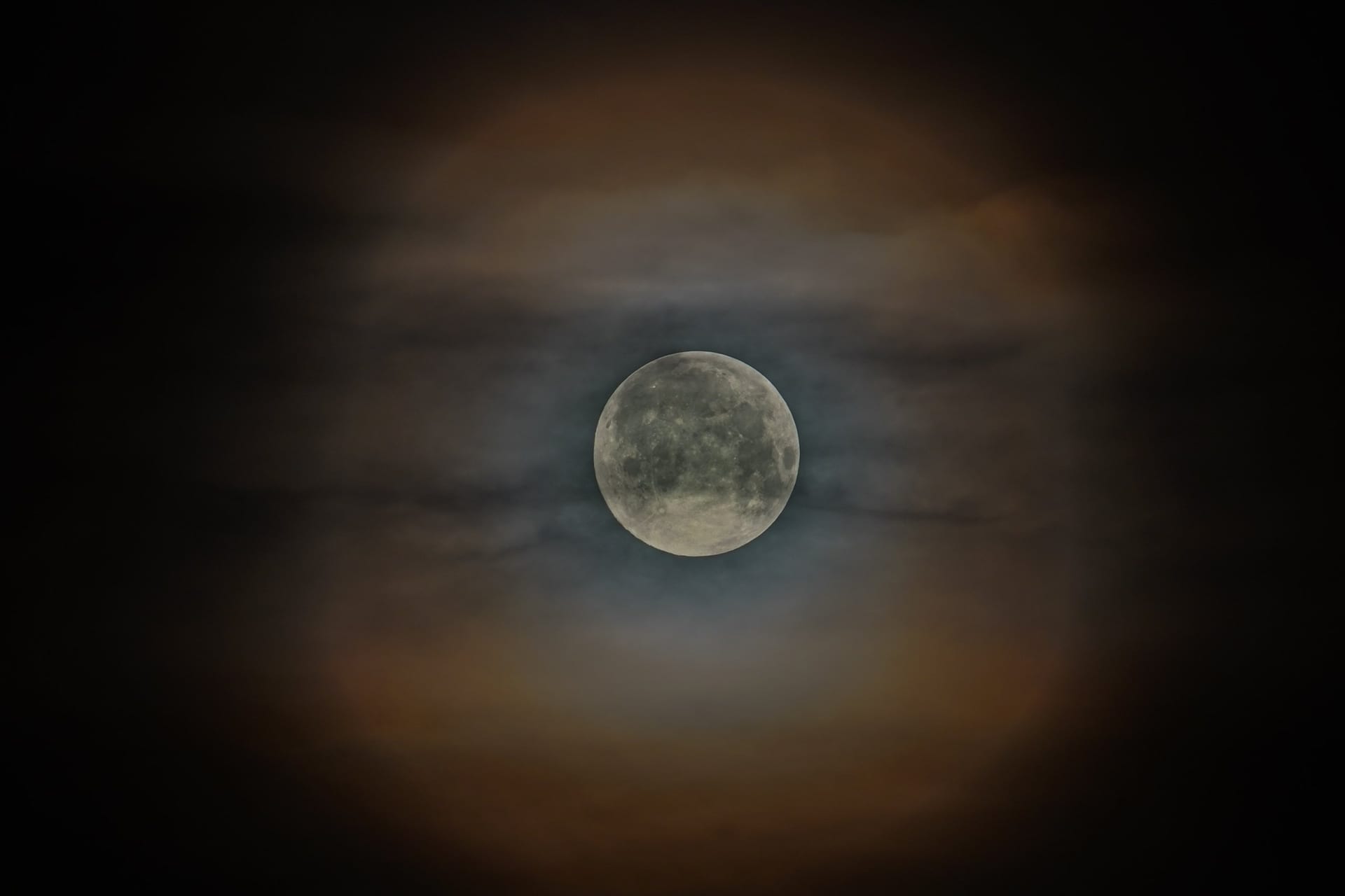 Fast voller Mond mit sichtbaren Kratern und Maria, umgeben von dünnen Wolkenschleiern am dunklen Nachthimmel.